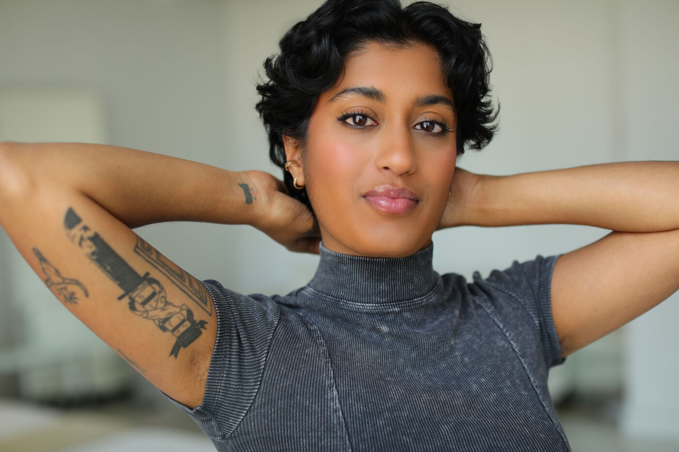 Headshot of Uma Paranjpe — hands behind head, tattoos visible