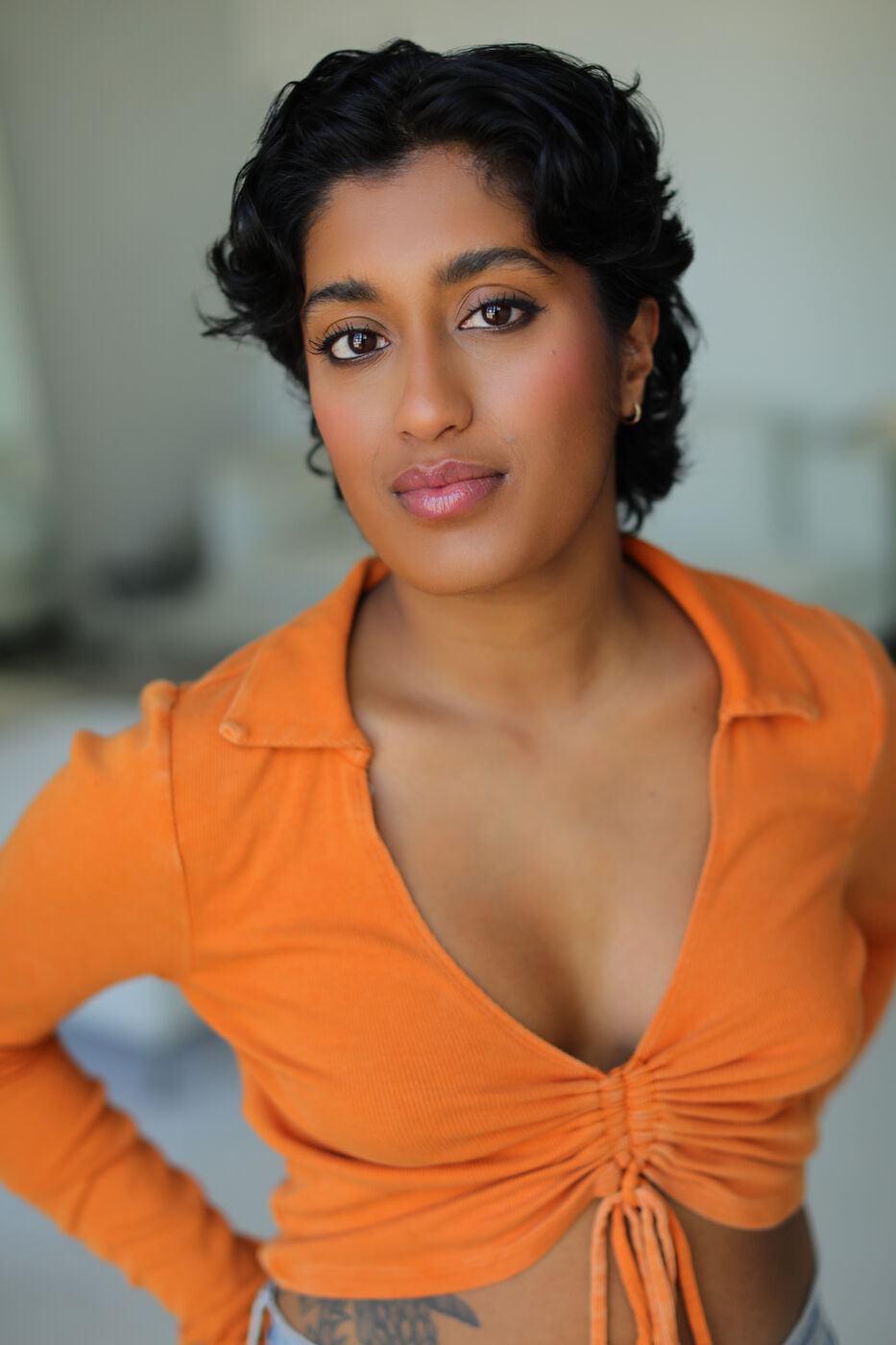 Headshot of Uma Paranjpe — orange top, hand on hip